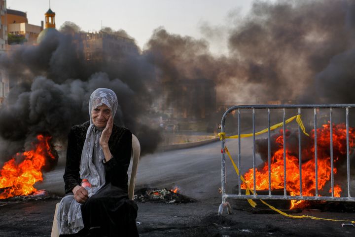 Ηλικιωμένη γυναίκα κάθεται μπροστά από τις φωτιές που έχουν ανάψει αντικυβερνητικοί διαδηλωτές (26 Ιουνίου 2021)