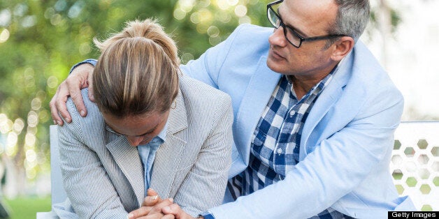 Hispanic mature couple sitting in a park bench, she is very sad and he is consoling her with his arms around her shoulders