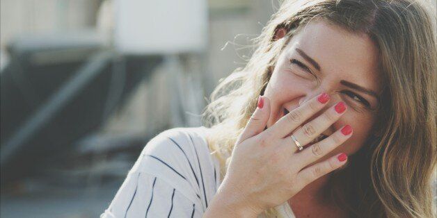 Young Woman Laughing While Hiding Mouth With Hand