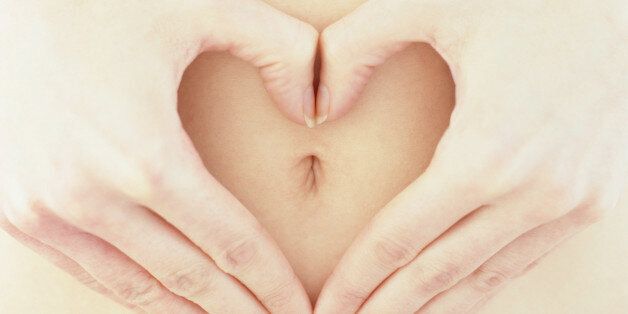Woman making heart shape with hands around belly button, close-up