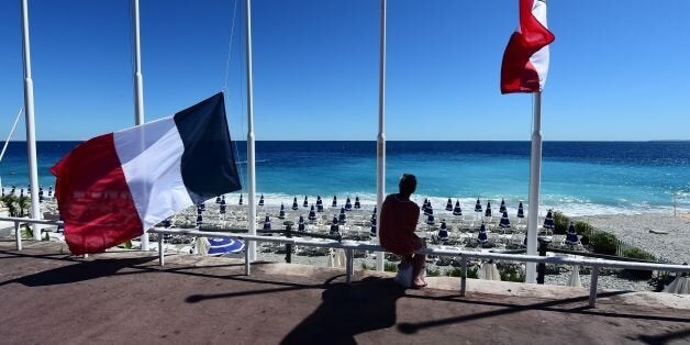 A woman sits under French flags lowered at half-mast in Nice on July 15, 2016, following the deadly Bastille Day attacks.
A