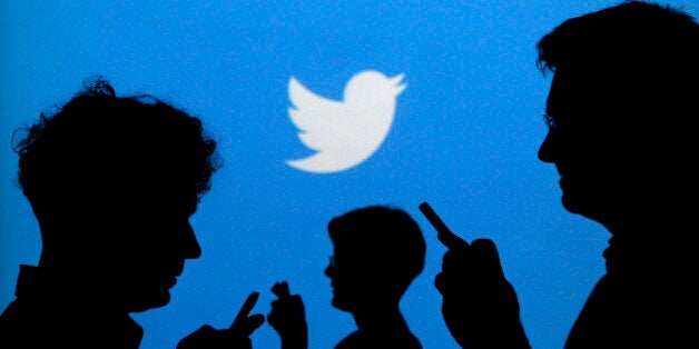 People holding mobile phones are silhouetted against a backdrop projected with the Twitter logo in this illustration picture