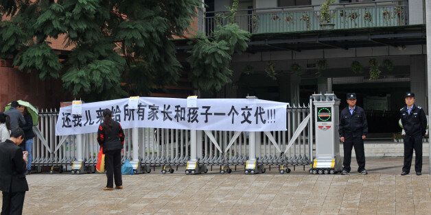 Guards (R) stand next to a banner with Chinese text which translates as 'Return my son! Explain to all parents and kids' displayed on the gate of a primary school on October 31, 2013, by family members after their child committed suicide in Chengdu, southwest China's Sichuan province. A 10-year-old Chinese boy allegedly committed suicide after he failed to write a self-criticism letter requested by his teacher, state media reported on October 31. CHINA OUT AFP PHOTO (Photo credit should read STR/AFP/Getty Images)