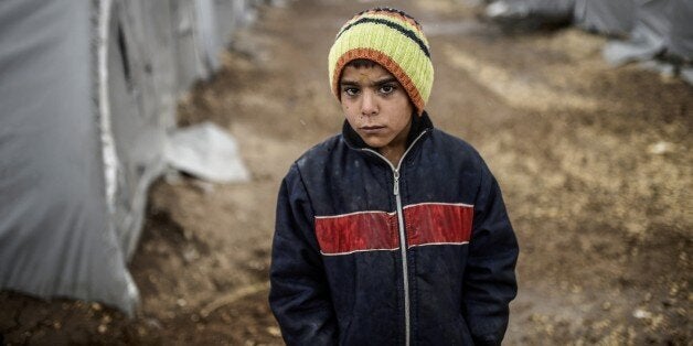 A Kurdish refugee boy stands during a rainy day at the Rojova Camp, in Suruc, a rural district of Sanliurfa Province, on October 30, 2014. Heavily armed Kurdish peshmerga fighters were on their way by land and by air, joining militias defending the Syrian border town of Kobane, also known as Ain al-Arab, from the Islamic State group after setting off from Iraq. Kobane's Kurdish defenders have been eagerly waiting for the peshmerga since Turkey last week said it would allow them to traverse its territory to enter the town. AFP PHOTO/ BULENT KILIC (Photo credit should read BULENT KILIC/AFP/Getty Images)