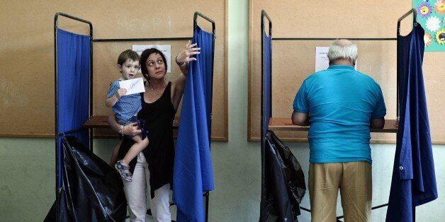 A boy holds his mother's vote as she exits a polling booth during the Greek referendum in Thessaloniki on July 5, 2015. Greek voters headed to the polls today to vote in a historic, tightly fought referendum on whether to accept worsening austerity in exchange for more bailout funds, in a gamble that could see it crash out of the euro. AFP PHOTO / SAKIS MITROLIDIS (Photo credit should read SAKIS MITROLIDIS/AFP/Getty Images)