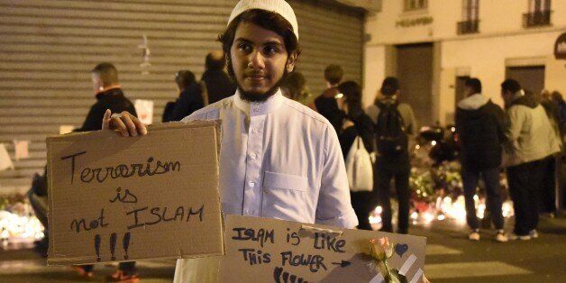 A muslim holds placard reading 'Terrorism is not Islam. Islam is like this flower. Terrorsim has no religion' during a gathering at 'Le Carillon' restaurant one of the site of the attacks in Paris, on November 15, 2015, in the 10th district of Paris. Islamic State jihadists claimed a series of coordinated attacks by gunmen and suicide bombers in Paris that killed at least 129 people in scenes of carnage at a concert hall, restaurants and the national stadium. AFP PHOTO / DOMINIQUE FAGET (Photo credit should read DOMINIQUE FAGET/AFP/Getty Images)