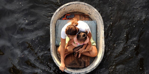 A mother and child travel inside a plastic tub as flood waters inundated a new residential area in Bangkok on November 7, 2011. According to experts Thai capital, built on swampland, is slowly sinking and the floods currently besieging Bangkok could be merely a foretaste of a grim future as climate change makes its impact felt. AFP PHOTO/ SAEED KHAN (Photo credit should read SAEED KHAN/AFP/Getty Images)