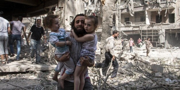 A Syrian man carries his two girls as he walks across the rubble following a barrel bomb attack on the rebel-held neighbourhood of al-Kalasa in the northern Syrian city of Aleppo on September 17, 2015. Once Syria's economic powerhouse, Aleppo has been ravaged by fighting since the rebels seized the east of the city in 2012, confining government forces to the west. AFP PHOTO / KARAM AL-MASRI / AFP / KARAM AL-MASRI (Photo credit should read KARAM AL-MASRI/AFP/Getty Images)