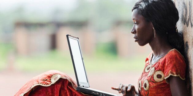 Street Shot of an African Ethnicity young woman working on business holding her technology item computer in a university in Bamako, Mali. Blurred background. University high school environment. 