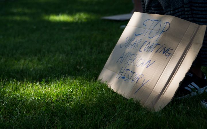 A sign reading "Stop sugarcoating American history" sits at the feet of demonstrators at a march against racism on June 19, 2020, at a high school in Milton, Massachusetts.