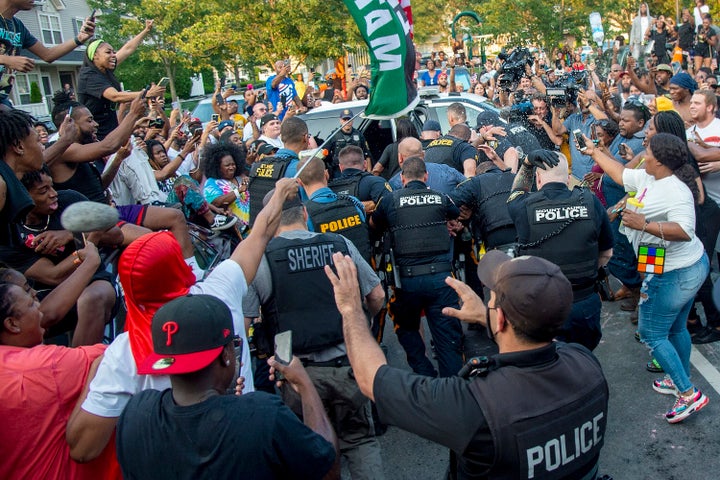 Police escort Edward Cagney Mathews through a crowd of people outside his Mount Laurel, New Jersey, home on Monday. 