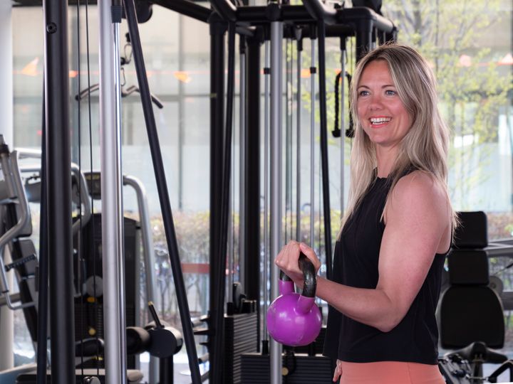 One woman, young blonde woman training with kettlebell in gym alone. Looking away.