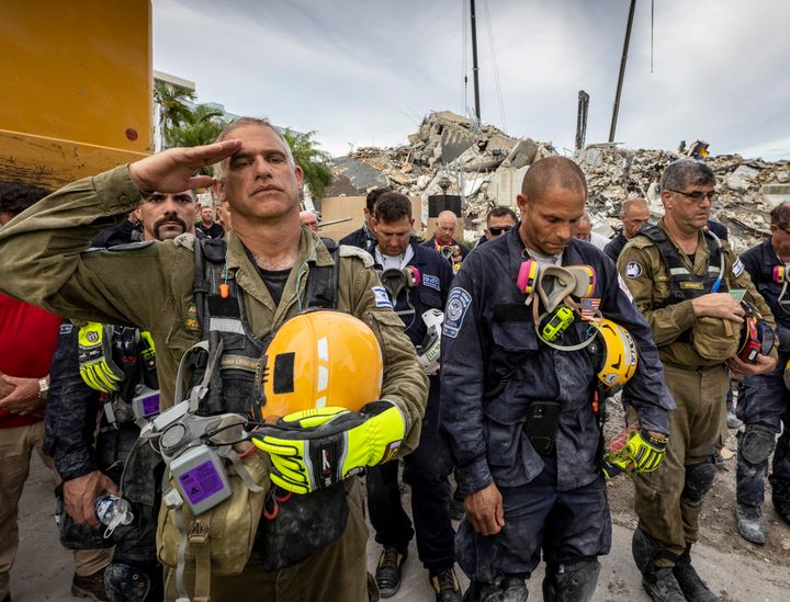 A member of the Israeli search and rescue team, left, salutes in front of the rubble that once was Champlain Towers South during a prayer ceremony on Wednesday in Surfside, Florida.