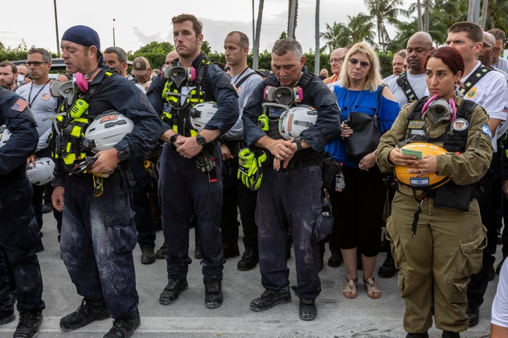 Members of a search and rescue team stand in front of the rubble that once was Champlain Towers South during a prayer ceremon