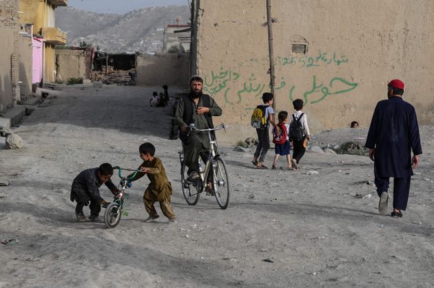 People pass by as children play with a cycle along a road at a residential area in Kabul on July 11,...