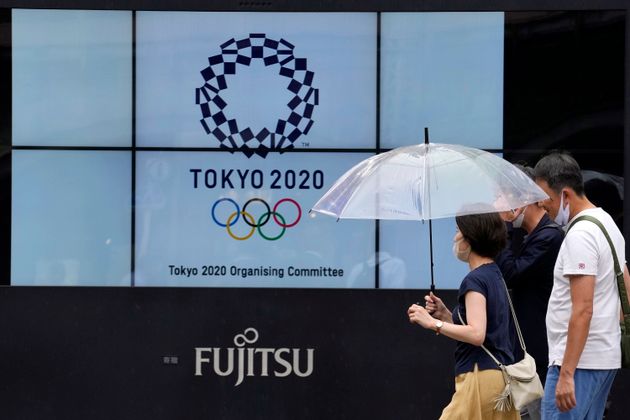Personas con cubrebocas pasan al lado del logo de los Juegos Olímpicos de 2020 cerca de la estación de trenes Shimbashi, en Tokio, el viernes 9 de julio de 2021. La cuenta regresiva es de 14 días. (AP Foto/Eugene Hoshiko)