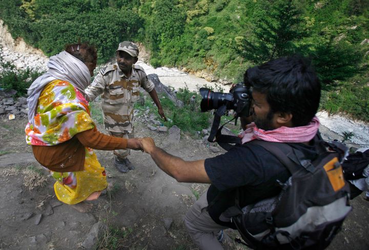 Reuters photographer Danish Siddiqui, right, takes photographs while helping a flood-affected woman who is being evacuated from the upper reaches of Govindghat, India, Sunday, June 23, 2013. Afghan government forces battled Friday to retake a border crossing with Pakistan from Taliban insurgents, and the Reuters news agency said one of its photographers was killed in the area. Reuters said Pulitzer Prize-winning photographer Siddiqui, who was embedded with the Afghan special forces, was killed Friday, July 16, 2021, as the commando unit sought to recapture Spin Boldak. (AP Photo/Rafiq Maqbool)
