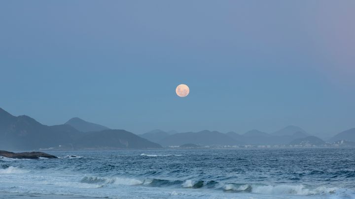 Rio de Janeiro, Brazil - February 8, 2020: View of the full moon rising above the mountain range landscape.