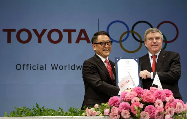 O πρόεδρος της Toyota, Άκιο Τογιόντα (αριστερά) και ο πρόεδρος της ΔΟΕ, Τόμας Μπαχ ποζάρουν στις κάμερες με την υπογεγραμμένη συμφωνία σε συνέντευξη Τύπου τον Μάρτιο του 2015. Την Δευτέρα 19 Ιουλίου η Toyota ανακοίνωσε πως δεν θα προβάλει τηλεοπτικές διαφημίσεις που θα σχετίζονται με τους Αγώνες στην ιαπωνική τηλεόραση.αν και είναι βασικός χορηγός της ΔΟΕ. (AP Photo/Eugene Hoshiko, File)