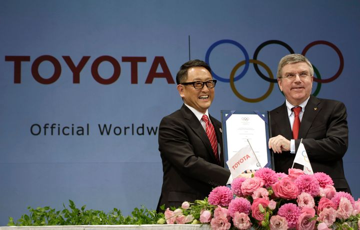 O πρόεδρος της Toyota, Άκιο Τογιόντα (αριστερά) και ο πρόεδρος της ΔΟΕ, Τόμας Μπαχ ποζάρουν στις κάμερες με την υπογεγραμμένη συμφωνία σε συνέντευξη Τύπου τον Μάρτιο του 2015. Την Δευτέρα 19 Ιουλίου η Toyota ανακοίνωσε πως δεν θα προβάλει τηλεοπτικές διαφημίσεις που θα σχετίζονται με τους Αγώνες στην ιαπωνική τηλεόραση.αν και είναι βασικός χορηγός της ΔΟΕ. (AP Photo/Eugene Hoshiko, File)