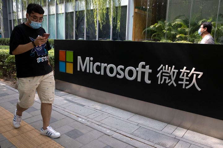 A man looks at his smartphone as he walks by the Microsoft office in Beijing, China on Friday, Aug. 7, 2020. (AP Photo/Ng Han
