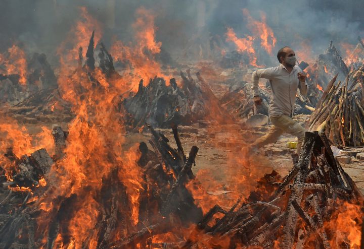 In this April 29, 2021, file photo, a man runs to escape heat emitting from the multiple funeral pyres of COVID-19 victims at