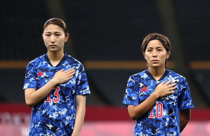 SAPPORO, JAPAN - JULY 21: (L - R) Yuzuho Shiokoshi #13 and Mana Iwabuchi #10 of Team Japan stand for the national anthem prior to the Women's First Round Group E match between Japan and Canada during the Tokyo 2020 Olympic Games at Sapporo Dome on July 21, 2021 in Sapporo, Hokkaido, Japan. (Photo by Masashi Hara/Getty Images)