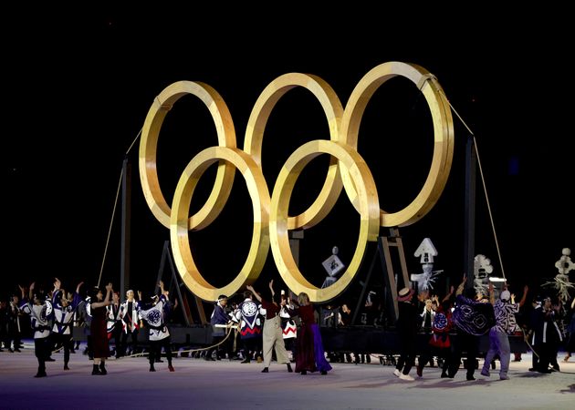 Performers dance in front of giant golden Olympic Rings.