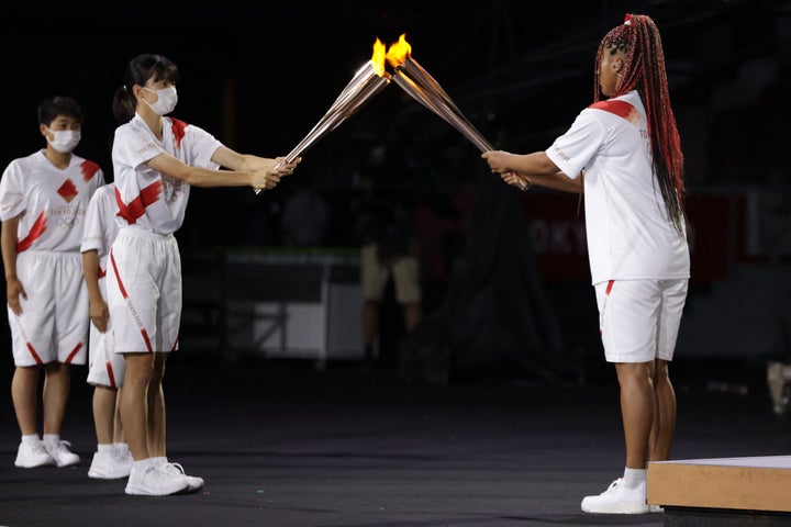 Japan's tennis player Naomi Osaka (R) lights her Olympic Torch before lighting the flame of hope in the Olympic Cauldron duri