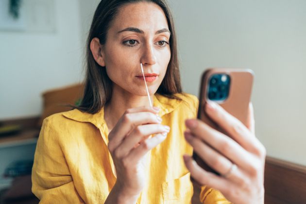 Young woman using Coronavirus nasal swab test at home in front of smartphone