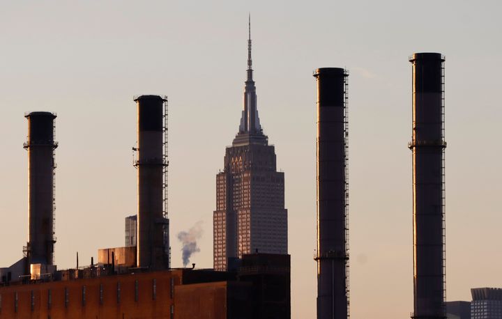 The sun sets on the Empire State Building as it sits behind smoke stacks of a ConEdison power plant.