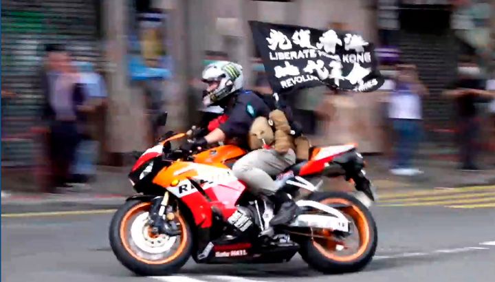 In this July 1, 2020, file image made from video, motorcyclist Tong Ying-kit carries a flag reading "Liberate Hong Kong, Revo