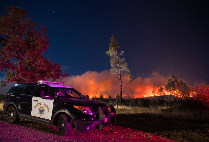 In this Sept. 28. 2020, file photo, a California Highway Patrol officer watches flames visible from the Zogg Fire near Igo, Calif. 