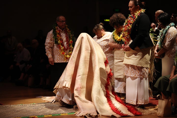 New Zealand Prime Minister Jacinda Ardern is covered by a mat of forgiveness during a service to make a formal apology to the