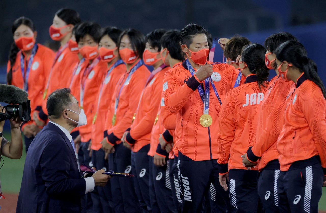 Softball player Yukiko Ueno of Japan (fourth from right) puts the gold medal on catcher Haruka Agatsuma (third from right) on the podium with other teammates, while medal presenter and Japan Olympic Committee President Yasuhiro Yamashita (lower left) looks on at the Yokohama Baseball Stadium in Yokohama, Japan, on July 27.