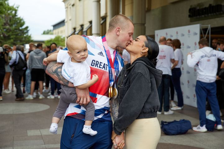 Adam Peaty kisses his wife Eirianedd Munro whilst holding their son George-Anderson Peaty at Heathrow Hotel on August 02, 2021 in London, England.