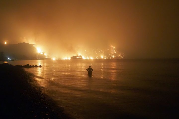 A man watches the flames as wildfire approaches Kochyli beach near Limni village on the island of Evia, about 160 kilometers (100 miles) north of Athens, Greece, late Friday, Aug. 6, 2021.