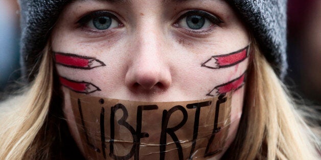 A woman has taped her mouth displaying the word Freedom on the tape, as she gathers with several thousand people in solidarity with victims of two terrorist attacks in Paris, one at the office of weekly newspaper Charlie Hebdo and another at a kosher market, front of the Brandenburg Gate near the French embassy in Berlin, Sunday, Jan. 11, 2015. in Berlin, Sunday, Jan. 11, 2015. (AP Photo/Markus Schreiber)