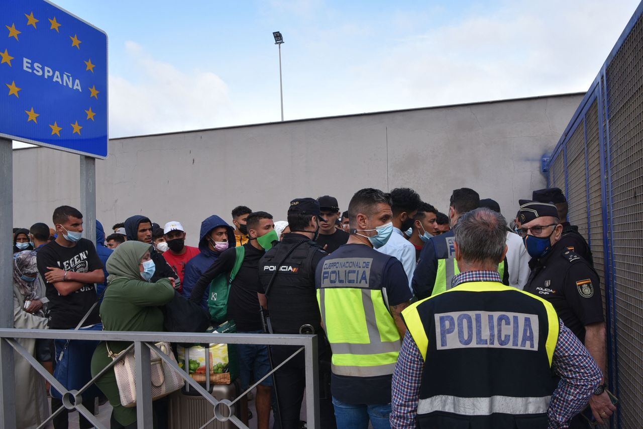 Spanish policemen stand next to migrants waiting to cross the border back to Morocco at the Spanish enclave of Ceuta on May 20, 2021