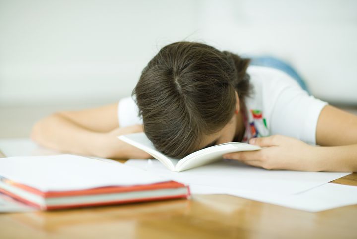 Teen girl lying on floor, doing homework, resting face in book