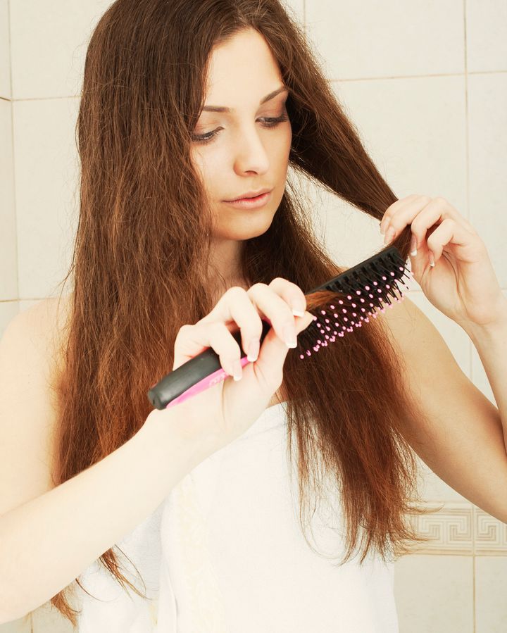 Young brunette lady combing her beautiful long hair in a bathroom