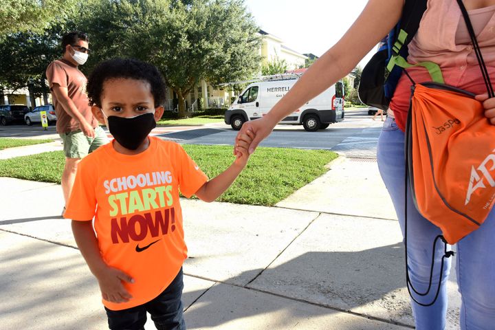 A young boy wears a face mask as he arrives with his mother on the first day of classes for the 2021-22 school year at Baldwin Park Elementary School in Orlando, Florida. Due to the surge in COVID-19 cases in Florida, Orange County public schools have implemented a face mask mandate for students for 30 days unless a parent chooses to opt out. 