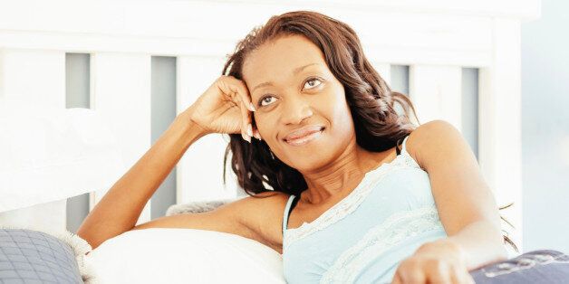 Young woman, relaxing on her bed, day-dreaming, smiling, thinking about something that makes her happy.