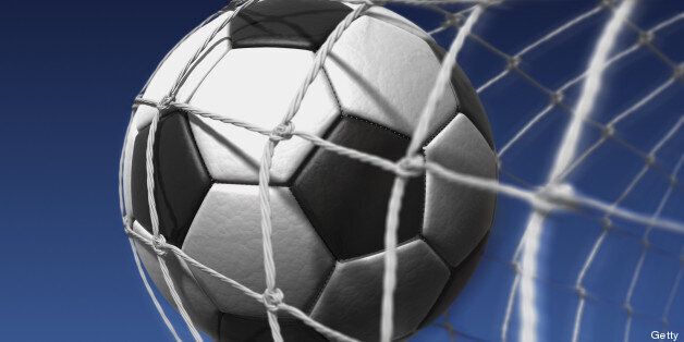 Scoring a Goal. A football/soccer ball hitting the back of the net. Close up against a blue sky