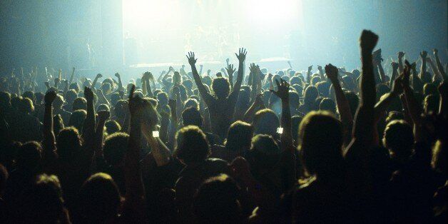 A general view of a rock concert taken from the back fo a venue showing the audience in silhouette raising their arms and cheering with bright lights shining from the stage, circa 1980. (Photo by Fin Costello/Redferns)