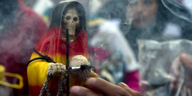 A devotee of the Santa Muerte (Saint of Death) blows smoke on an effigy during the main celebration at the marketof one of the most dangerous neighborhoods, known as Tepito in Mexico City, on November 1, 2012. Santa Muerte is an occult figure venerated primarily in Mexico and the United States, probably a syncretism between Mesoamerican and Catholic beliefs, although strongly condemned by the Catholic Church as Satanic. AFP PHOTO / YURI CORTEZ (Photo credit should read YURI CORTEZ/AFP/Getty Images)
