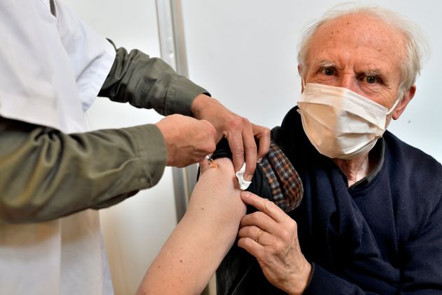 Une infirmière injecte à une personne agée portant un masque le vaccin Pfizer-BioNTech...