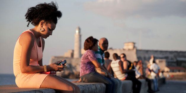 In this March 11, 2014 photo, a woman uses her cellphone as she sits on the Malecon in Havana, Cuba. The U.S. Agency for International Development masterminded the creation of a "Cuban Twitter," a communications network designed to undermine the communist government in Cuba, built with secret shell companies and financed through foreign banks, The Associated Press has learned. The project, which lasted more than two years and drew tens of thousands of subscribers, sought to evade Cubas stranglehold on the Internet with a primitive social media platform. (AP Photo/Franklin Reyes)
