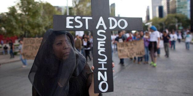 A woman wears a black veil and carries a cross reading in Spanish "Assassin State," as thousands march down one of the capital's main boulevards to demand that the government find the 43 students who disappeared in southern Guerrero State, in Mexico City, Wednesday, Oct. 8, 2014. Investigators still had no word on whether the 28 bodies found in a mass grave over the weekend included any of the missing students, who disappeared after two attacks allegedly involving Iguala police in which six people were killed and at least 25 wounded. (AP Photo/Rebecca Blackwell)