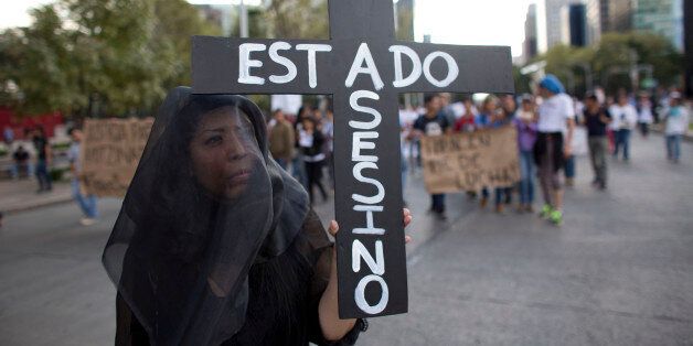 A woman wears a black veil and carries a cross reading in Spanish "Assassin State," as thousands march down one of the capital's main boulevards to demand that the government find the 43 students who disappeared in southern Guerrero State, in Mexico City, Wednesday, Oct. 8, 2014. Investigators still had no word on whether the 28 bodies found in a mass grave over the weekend included any of the missing students, who disappeared after two attacks allegedly involving Iguala police in which six people were killed and at least 25 wounded. (AP Photo/Rebecca Blackwell)